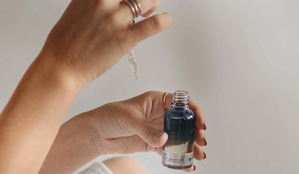 Close-up of hands using a dropper to add ammonia from a small bottle into an aquarium preparation setup, illustrating careful dosing.