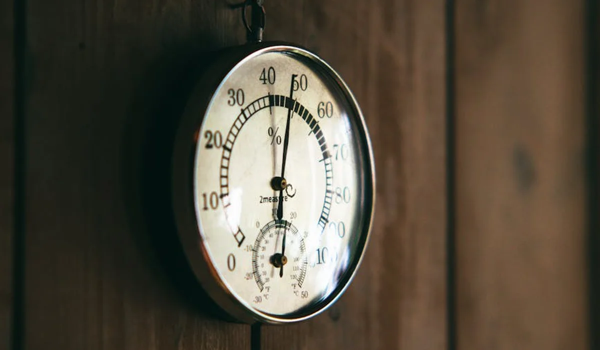 Round analog thermometer and hygrometer mounted on a wooden wall, showing multiple scales and a large dial.