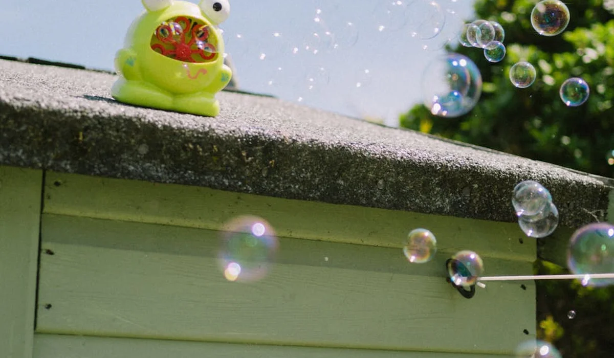 Green toy duck on a ledge with bubbles floating in front of a garden background