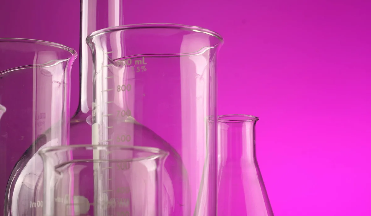 Lab glassware including beakers and flasks against a pink background, representing aquarium water testing