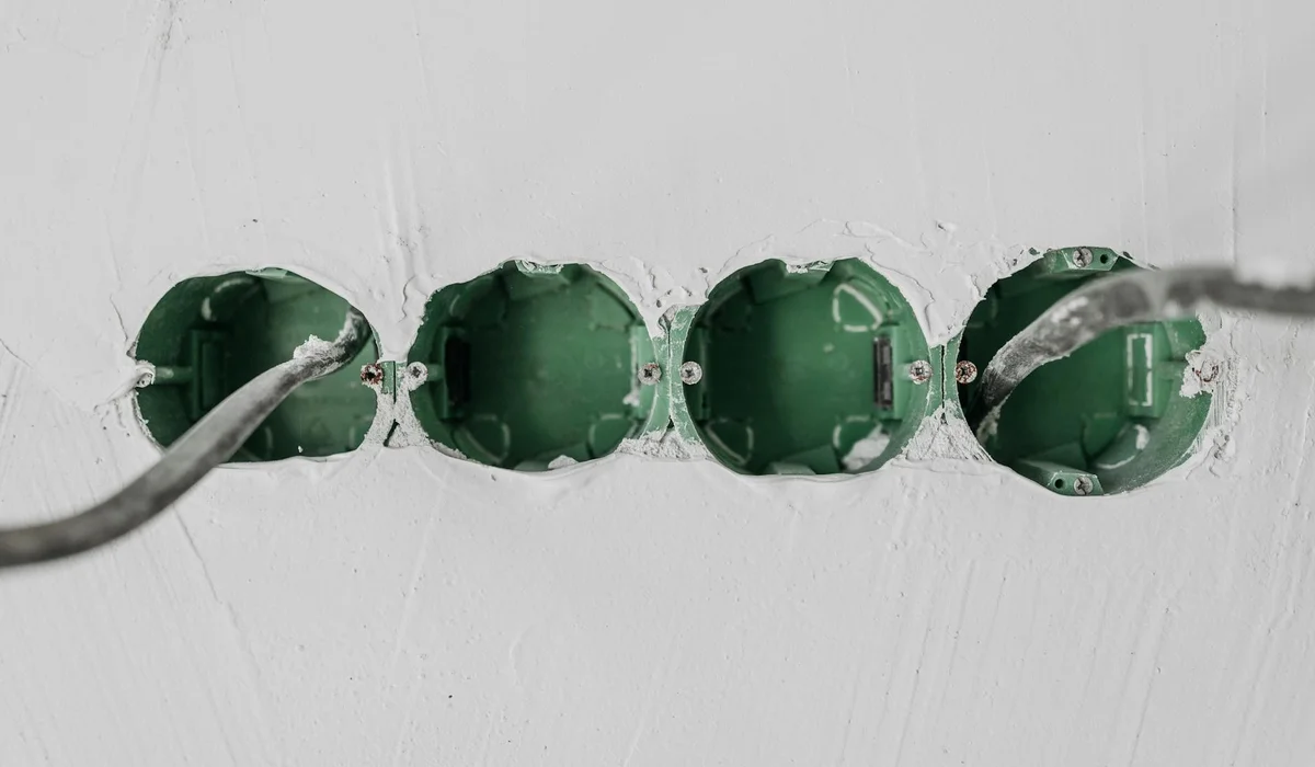 Row of four green circular electrical boxes with cables entering, mounted on a white wall; exposed wiring and openings suggest moisture risk near water.