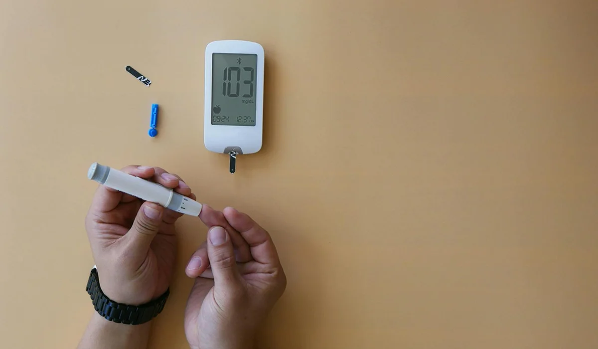 Hands holding an aquarium test strip near a digital reader on a beige surface