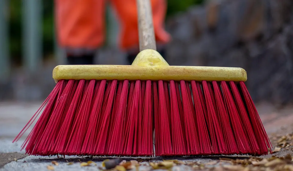 Red-bristled broom with a yellow handle lying on a paved surface.