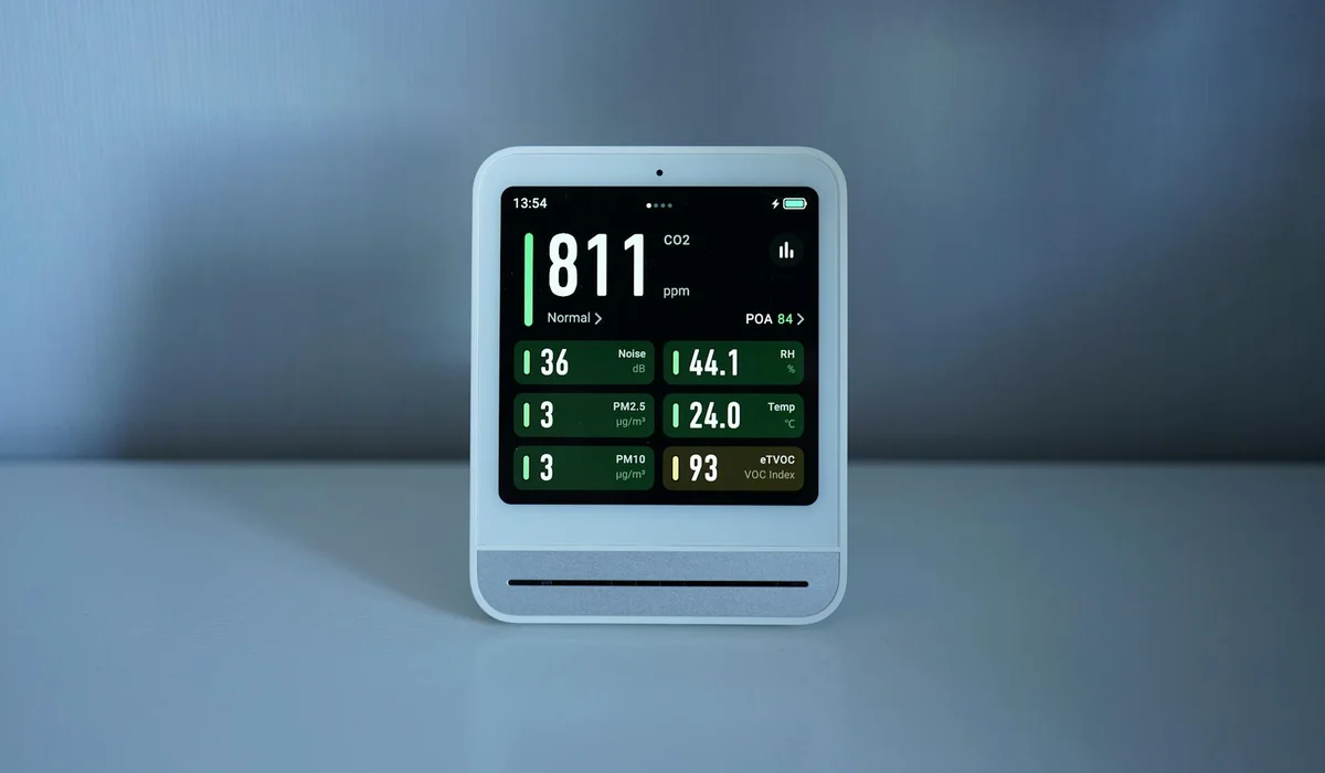 A compact digital CO2 monitor on a light surface displaying CO2 ppm and other readings on its screen.