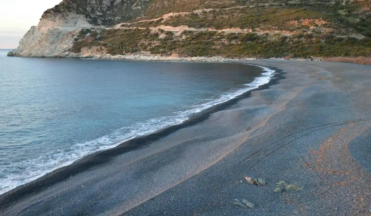 Coastal landscape with dark sand and a cliff, suggesting natural substrate textures for aquarists.