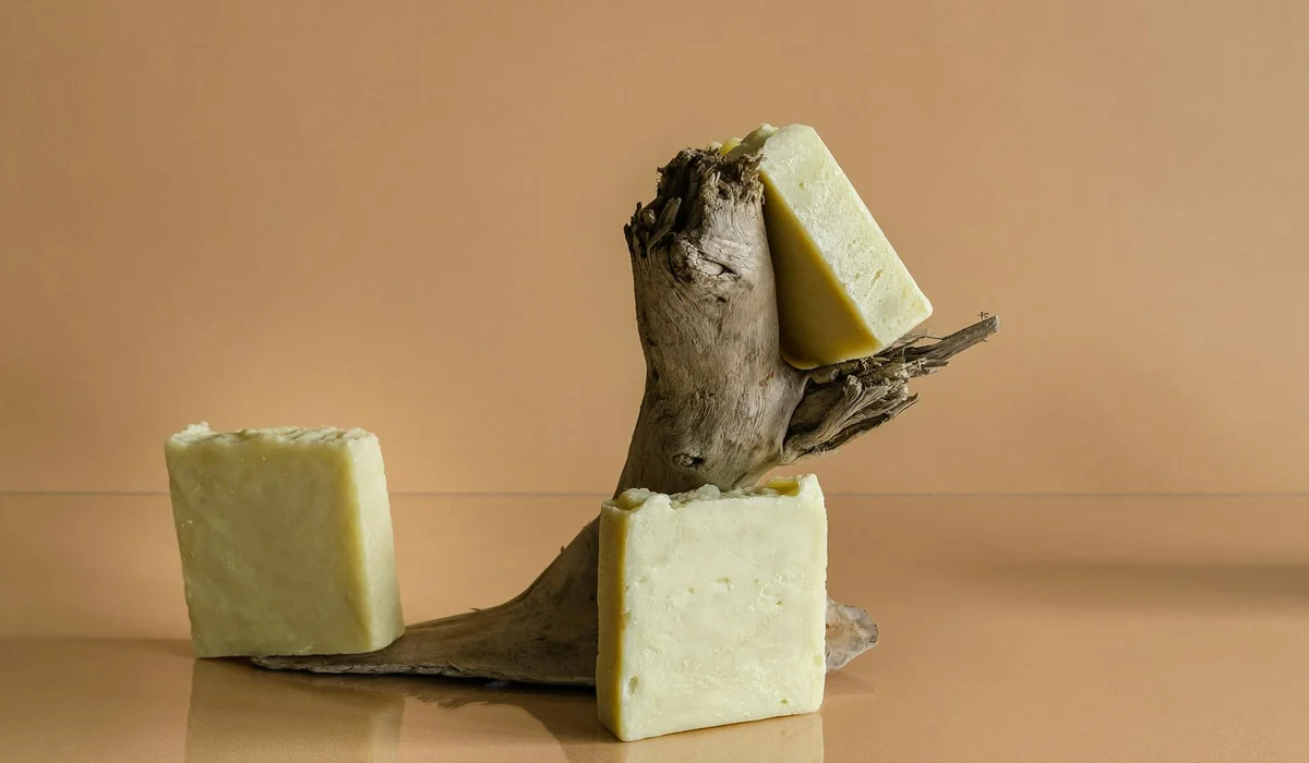 A piece of driftwood balanced against three pale-yellow rectangular blocks on a warm brown backdrop.