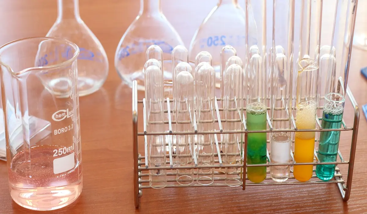 Beaker with pink liquid beside a rack of test tubes containing colored reagents for aquarium water testing in a laboratory.