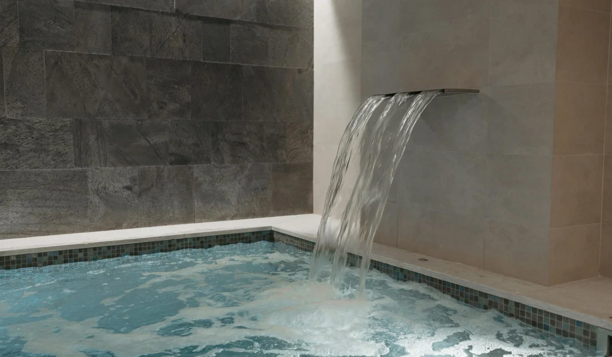Modern indoor pool with a cascading waterfall from a stone wall into a tiled basin, illustrating water circulation and flow.