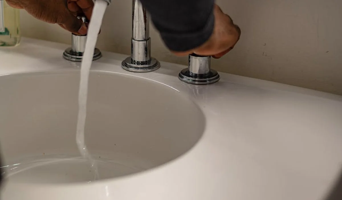 Close-up of a hand turning on a faucet over a sink, with water running into the basin, illustrating water preparation for an aquarium.