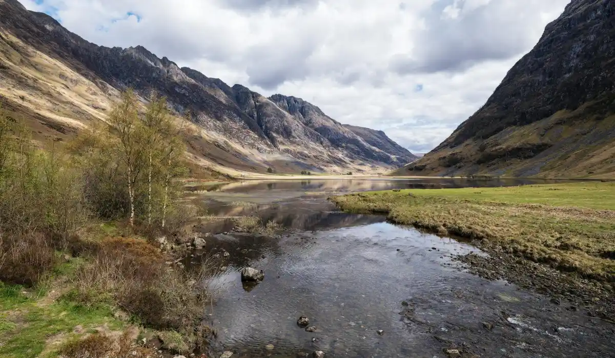 Mountain valley with a river running through trees and bare hills under a cloudy sky