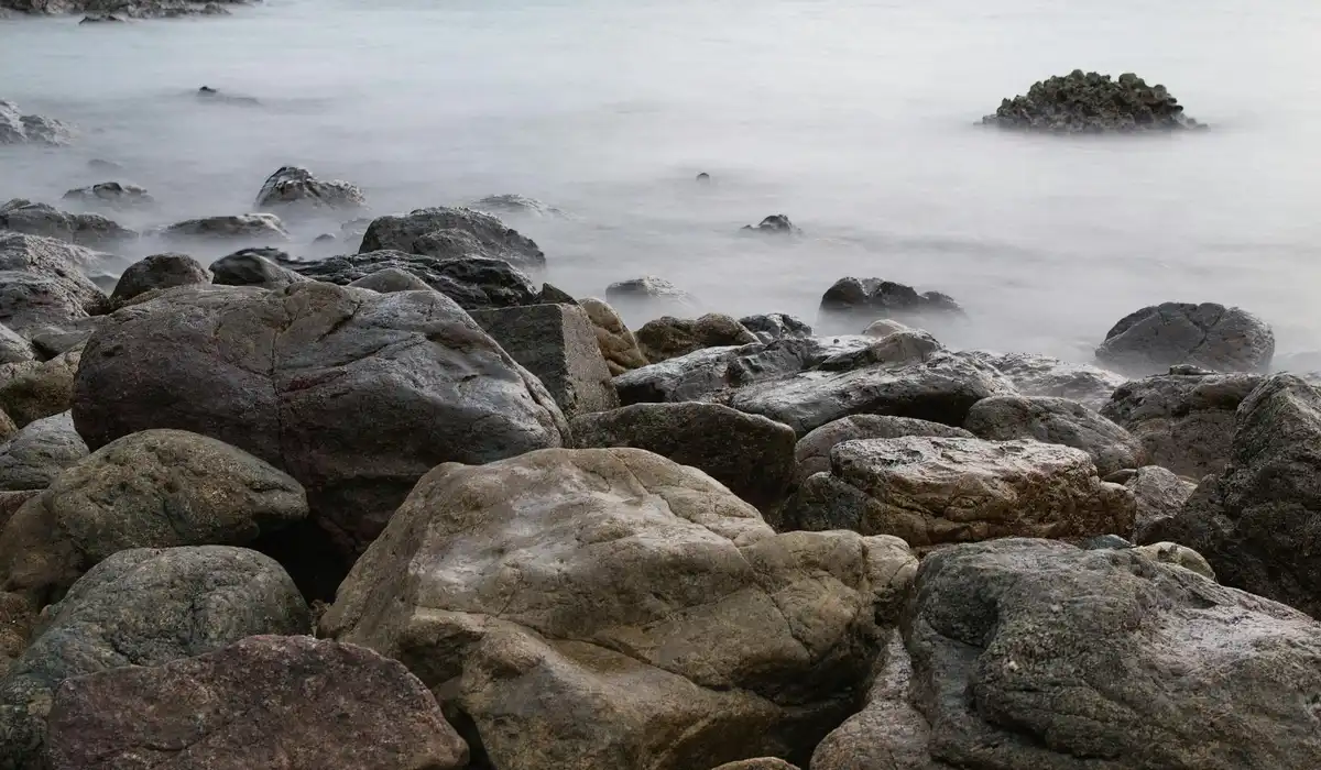 Rugged rocky shoreline with misty water in the distance.