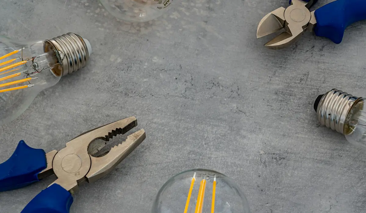 Blue-handled pliers and light bulbs on a gray workspace, representing electrical tools for monitoring aquarium energy consumption.