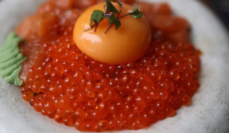 Close-up of bright red fish eggs (roe) arranged around an orange garnish on a white surface
