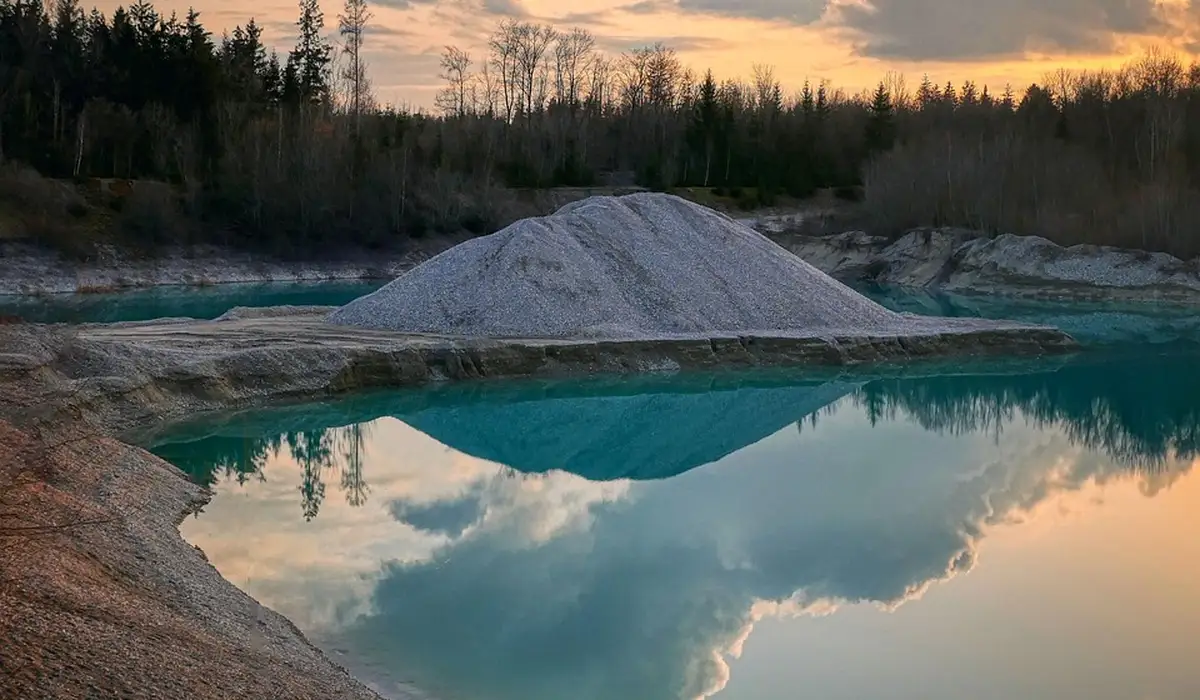 Turquoise water body with a white mineral pile on the shore, reflecting the sky and surrounding trees.