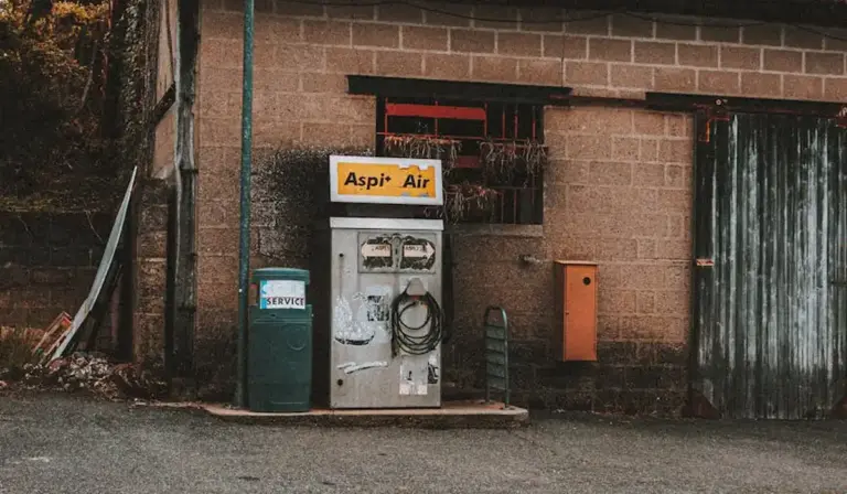 Old vintage gas pump outside a brick building with a weathered exterior and a green trash bin nearby.