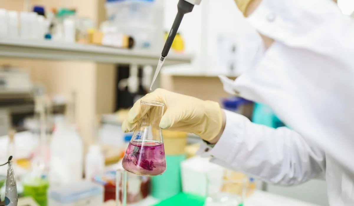 Laboratory scene showing a scientist using a pipette to transfer liquid into a conical flask to illustrate testing water parameters.