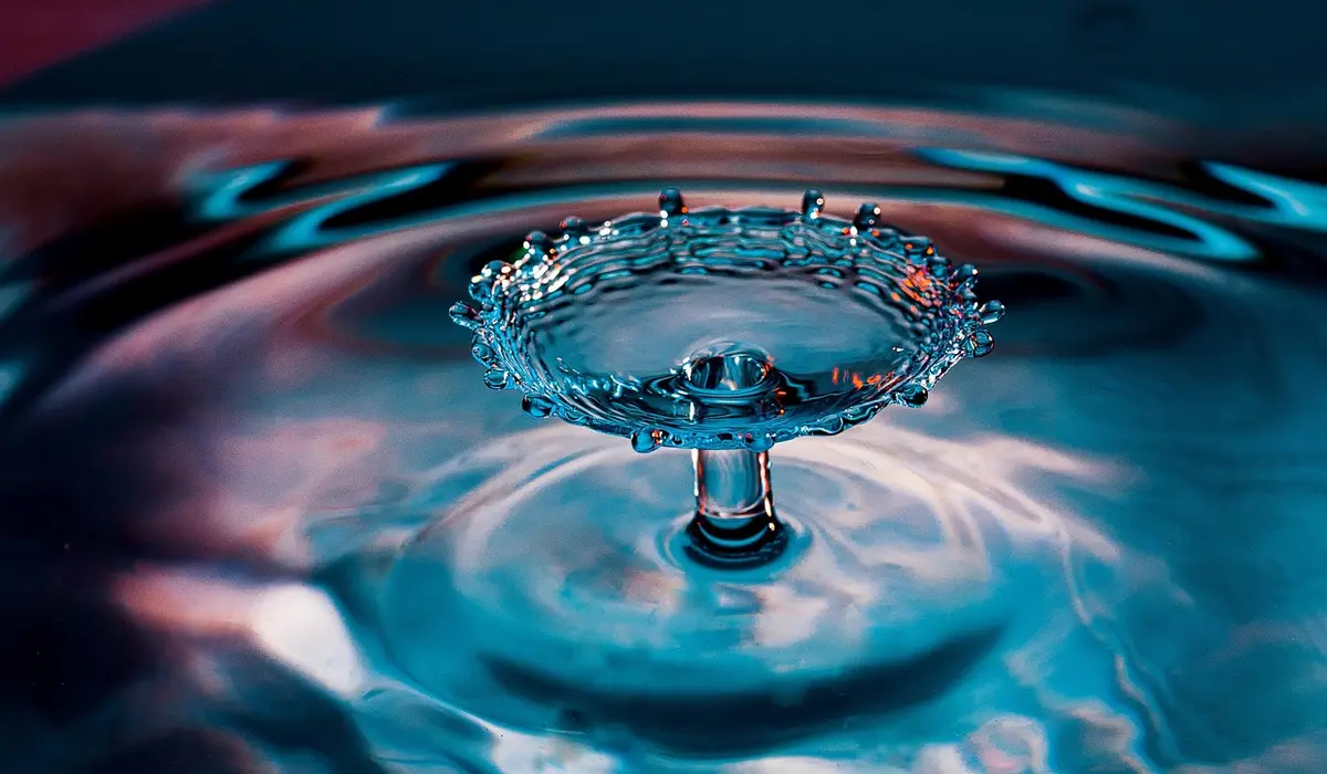 Close-up of a water droplet creating a crown-shaped splash on the surface of blue-tinted aquarium water.