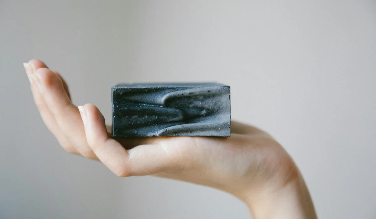 A hand holding a rectangular chunk of activated carbon with a smooth, charcoal-like surface against a neutral background.