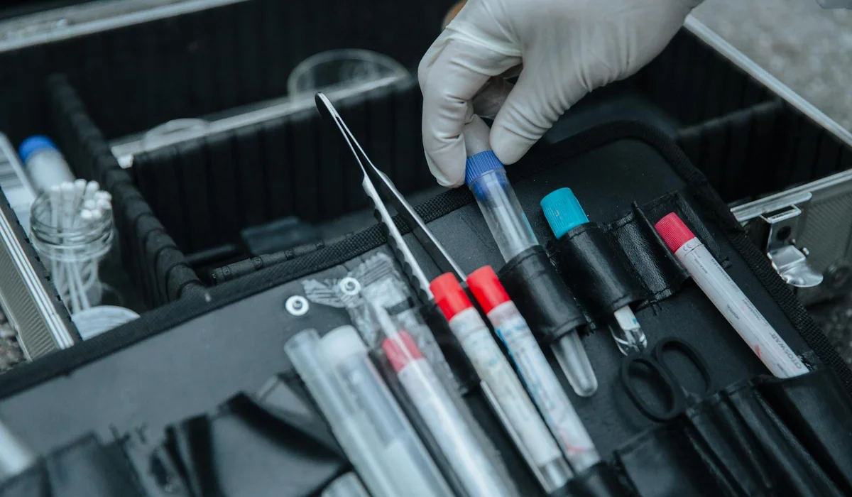 Gloved hand handling a pipette among aquarium water-testing tools inside a toolkit.