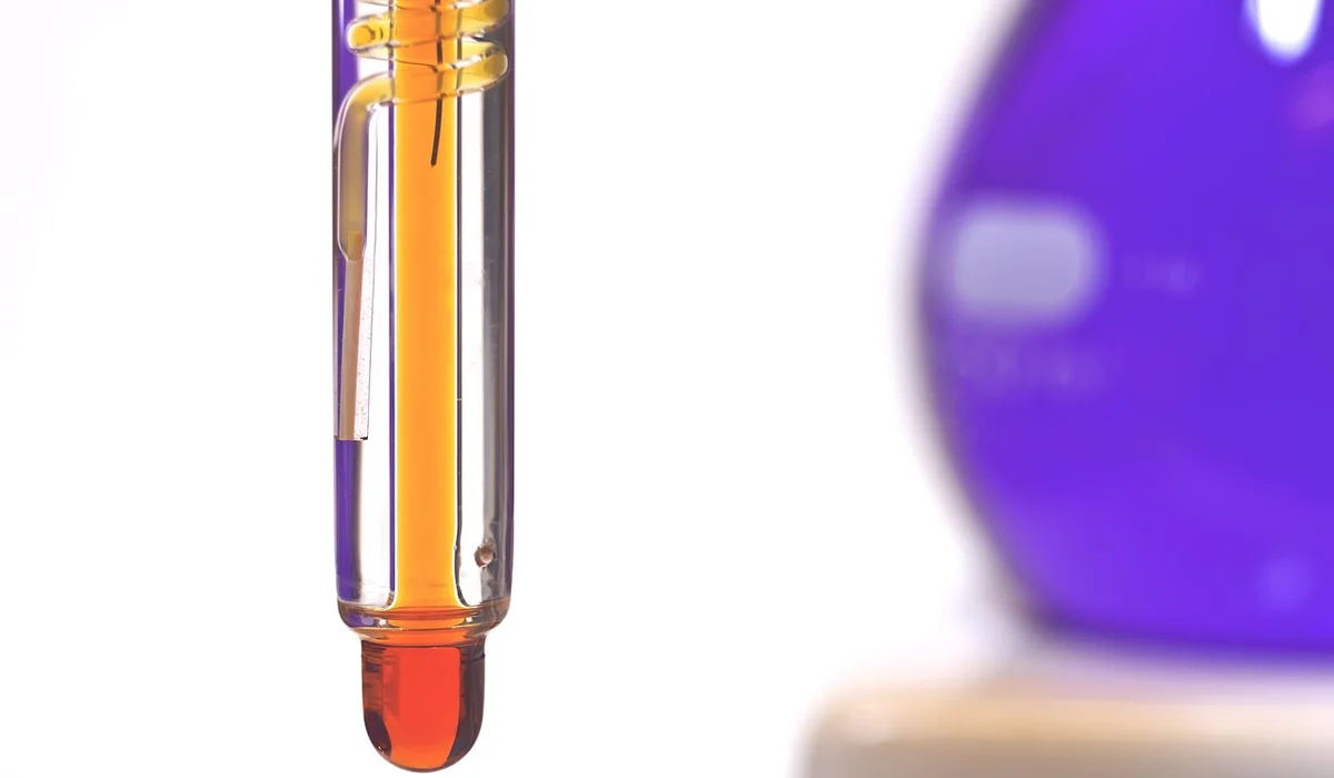 Close-up of a glass thermometer with orange liquid in an aquarium setting, with a blurred purple object in the background.