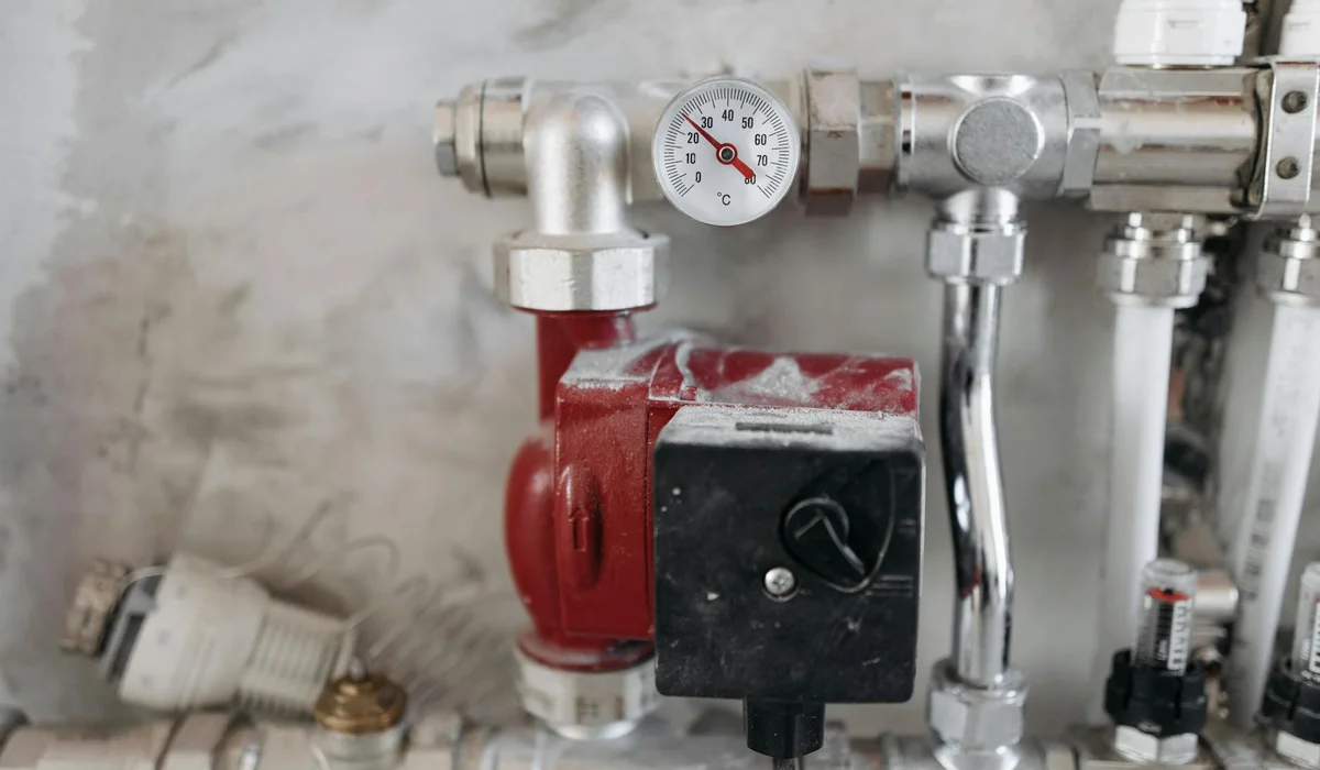 Close-up of an aquarium pump with a red motor housing, pressure gauge, and PVC plumbing fittings.