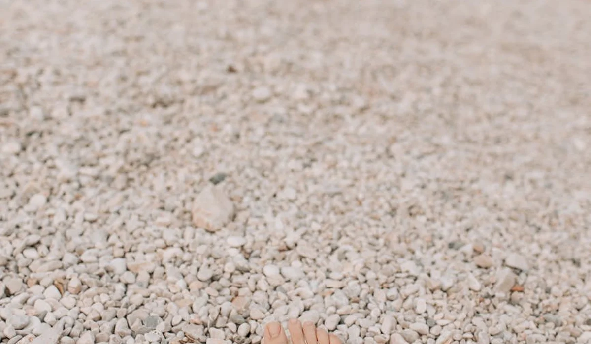 Close-up image of a pale gravel aquarium substrate with a small portion of a toe visible at the bottom.