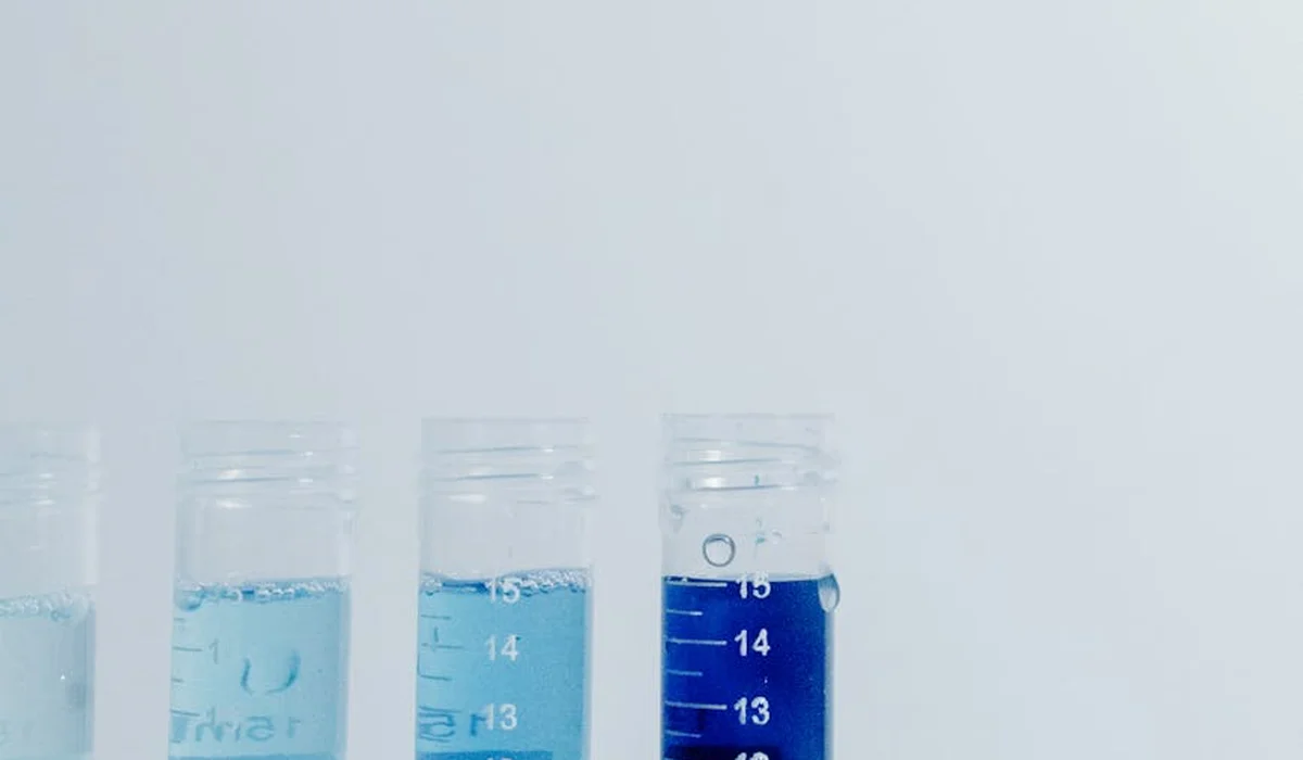 Row of aquarium water testing tubes with blue liquid against a pale background.
