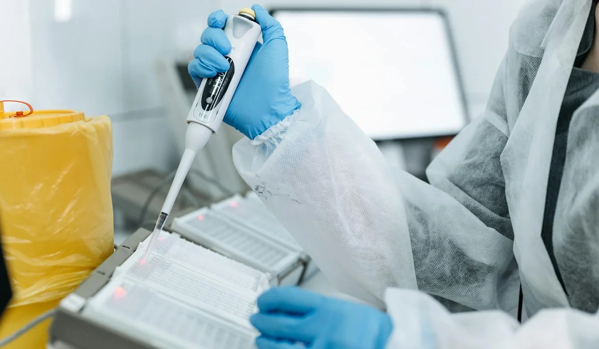 Lab technician wearing protective gloves and a lab coat uses a handheld pipette to load a test kit for aquarium water analysis.