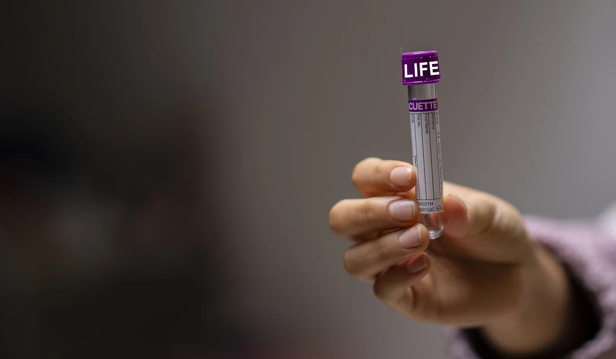 Close-up of a hand holding a small glass test tube with a purple cap, used for aquarium water testing