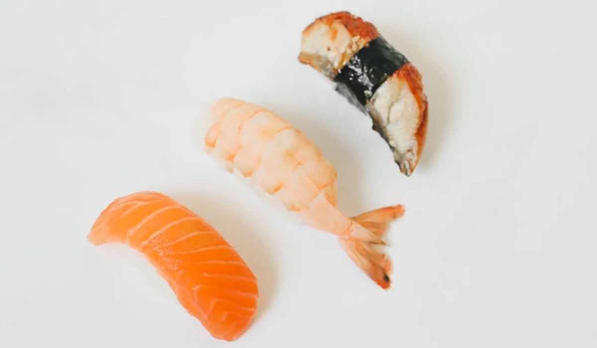 Three pieces of sushi on a white background: salmon nigiri, shrimp nigiri, and a nigiri with orange topping.
