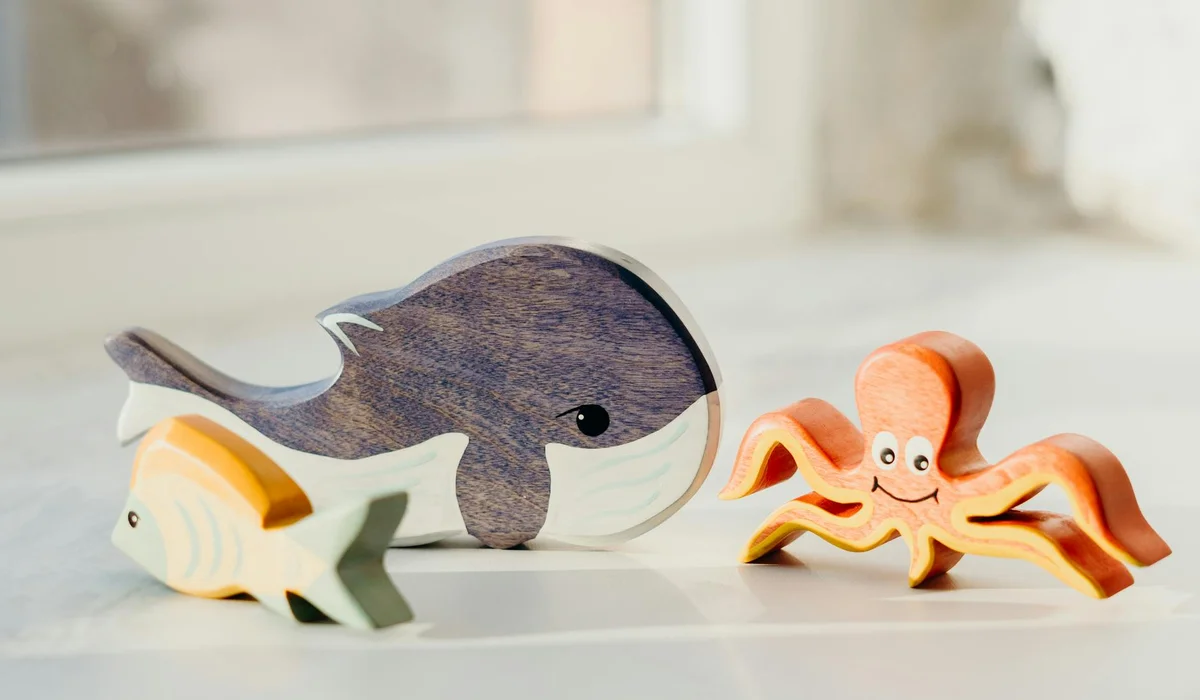 Wooden toy sea creatures, including a large whale, a small starfish, and an orange octopus, arranged on a light surface.