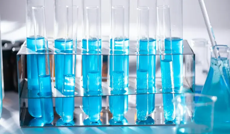 Test tubes filled with blue liquid in a glass rack on a laboratory bench.