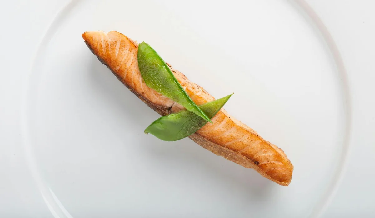 A small piece of baguette with a green leaf on a plain white plate.