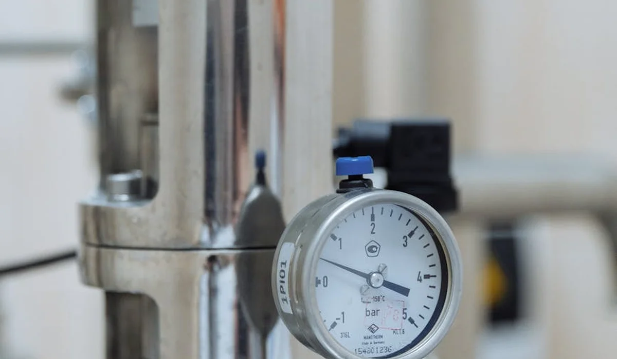 Close-up of a CO2 regulator gauge attached to a metal pipe in a planted aquarium setup.