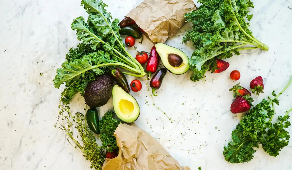 Fresh greens and vegetables (kale, avocado, cherry tomatoes, peppers) arranged on a light marble surface, illustrating ingredients for DIY snail meals.