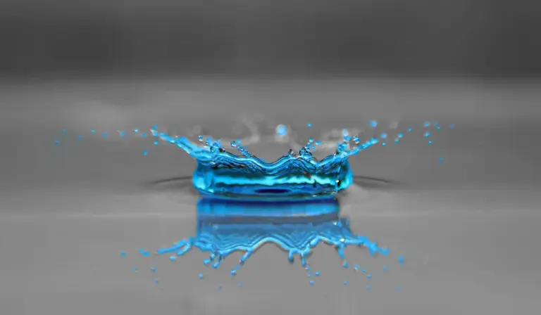 Blue water splash forming a crown above a gray surface, symbolizing distilled water in aquariums.