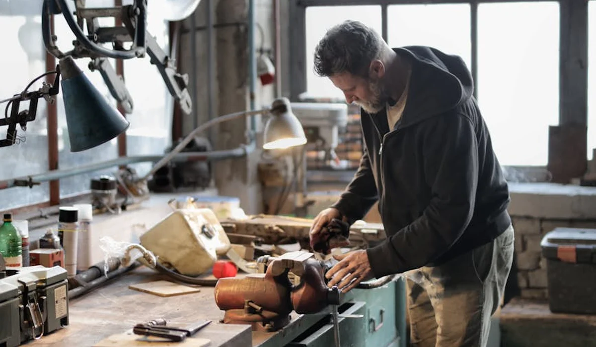 A woodworker in a cluttered workshop shapes a wooden frame for a DIY aquarium stand at a workbench.