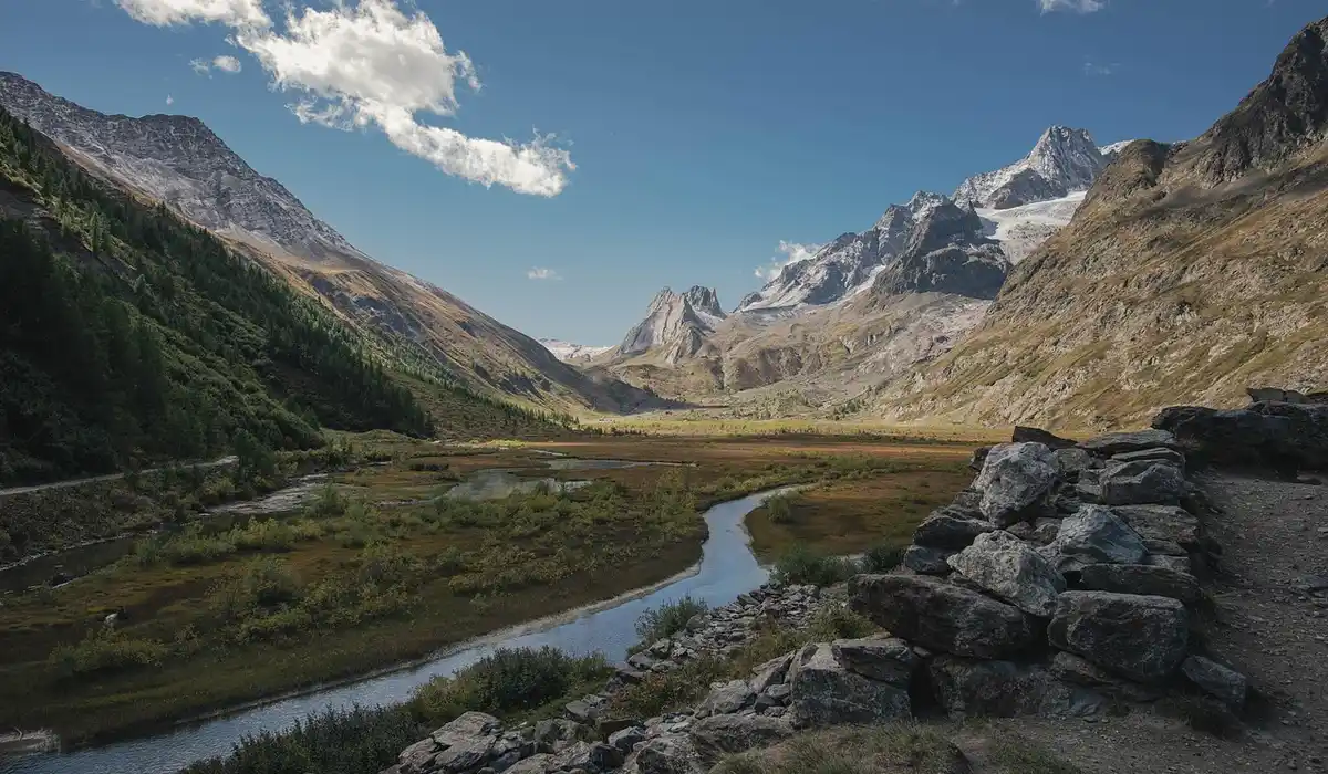A rugged valley with a winding stream, rocky banks, and distant snow-capped mountains, illustrating a natural riverbed scene for hillstream loach aquascapes.