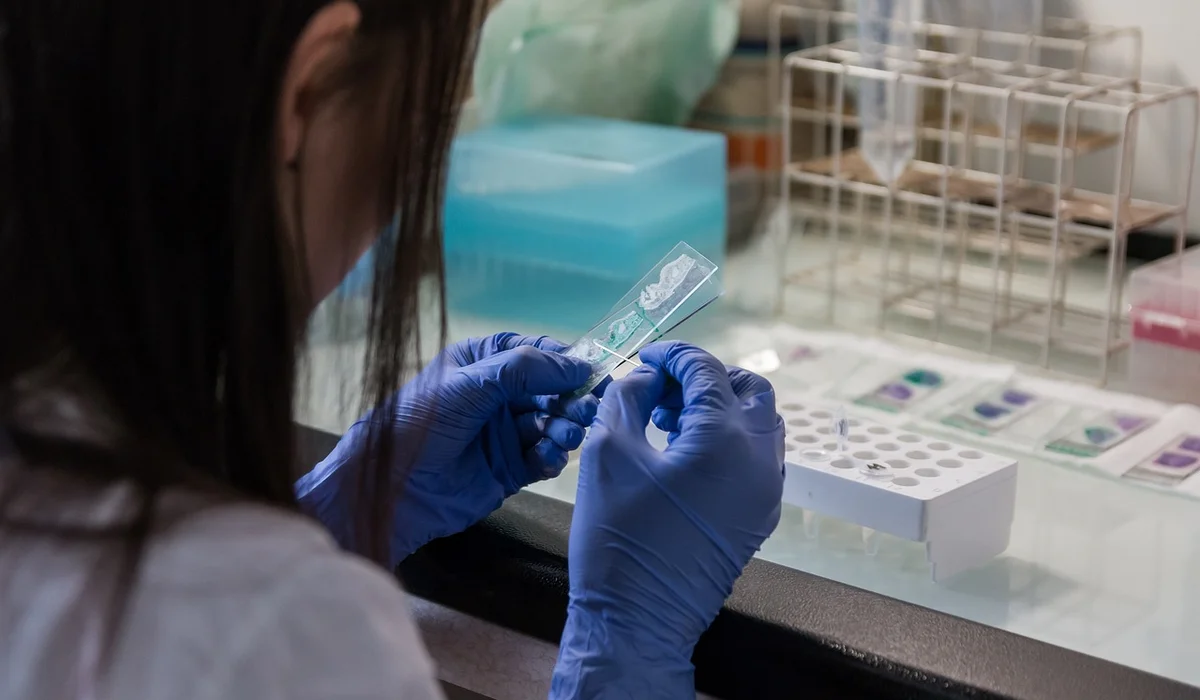 A lab technician wearing blue gloves handling an ammonia test kit at a laboratory bench, preparing to test aquarium water.