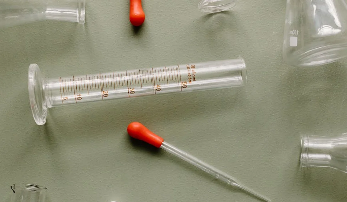 Close-up of glass test tubes and droppers with red rubber bulbs on a green surface, used for aquarium water testing