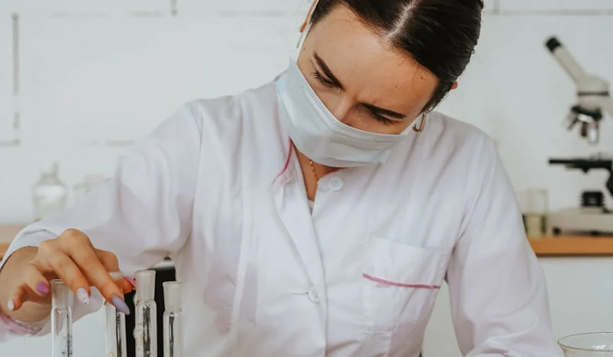 Lab technician wearing a white coat and mask examines test tubes in a laboratory, illustrating careful water preparation
