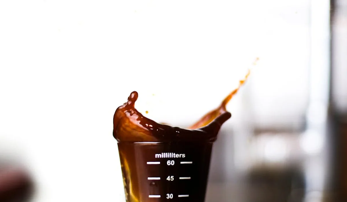 Close-up of a measuring cup with dark liquid and milliliter markings, illustrating measurement of water volume.