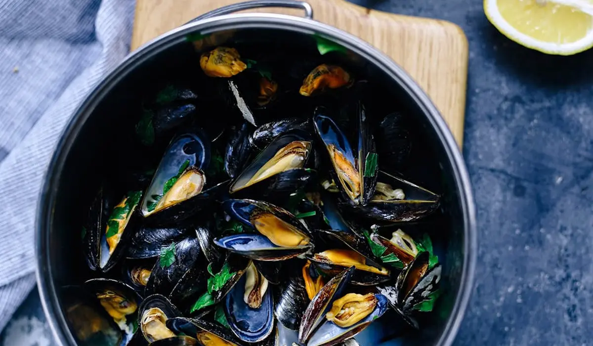 A pot filled with opened mussels on a dark surface, with a lime wedge nearby.