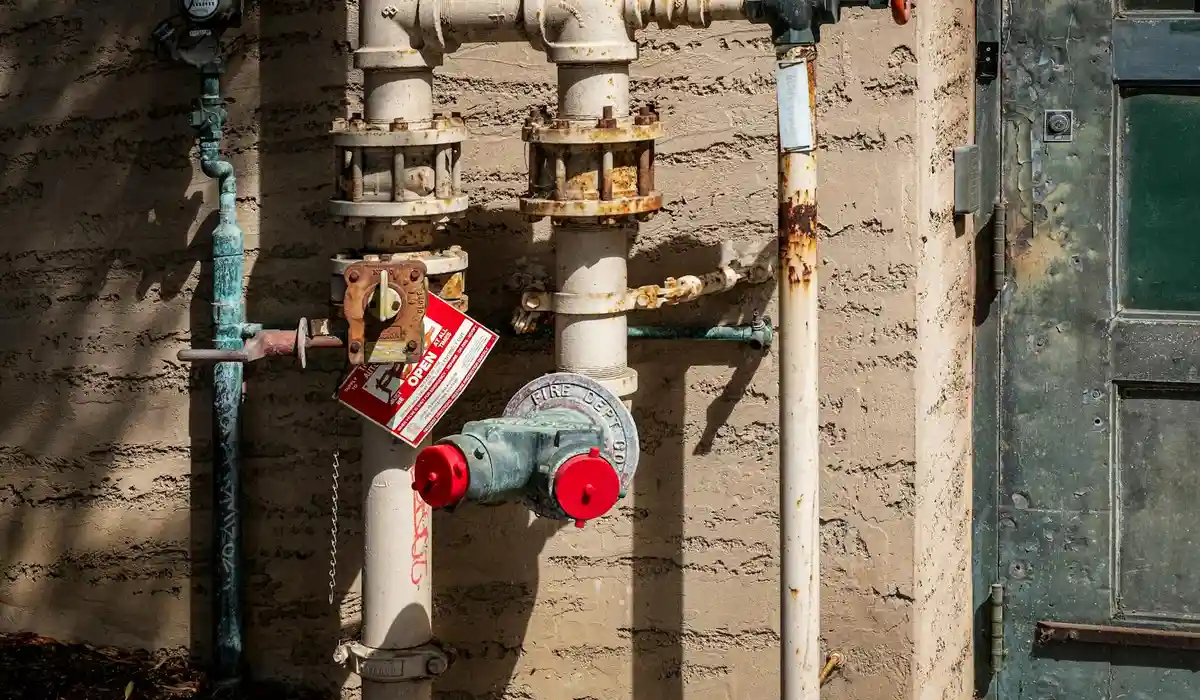 Close-up of outdoor plumbing pipes with valves and a round gauge mounted on a brick wall