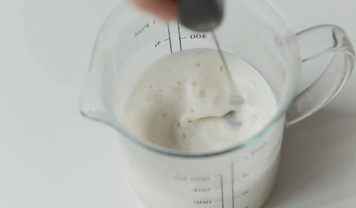 Close-up of a glass measuring beaker filled with a milky liquid and a dropper held above, showing measurement marks on the side.