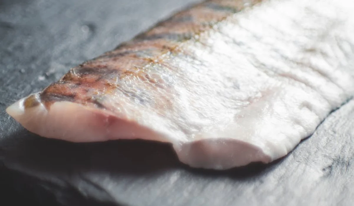Close-up of a raw fish fillet on a wooden cutting board.