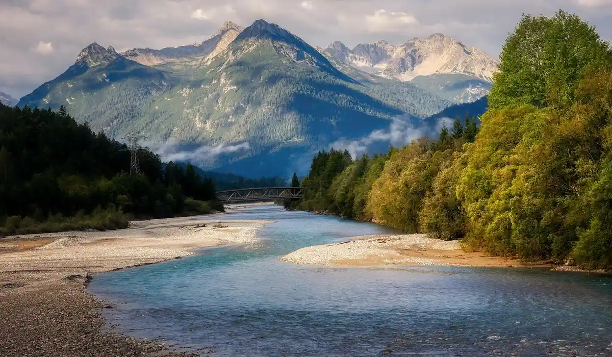 River landscape with mountains, trees along the banks, and a calm stream—visual metaphor for careful water management in aquarium maintenance.