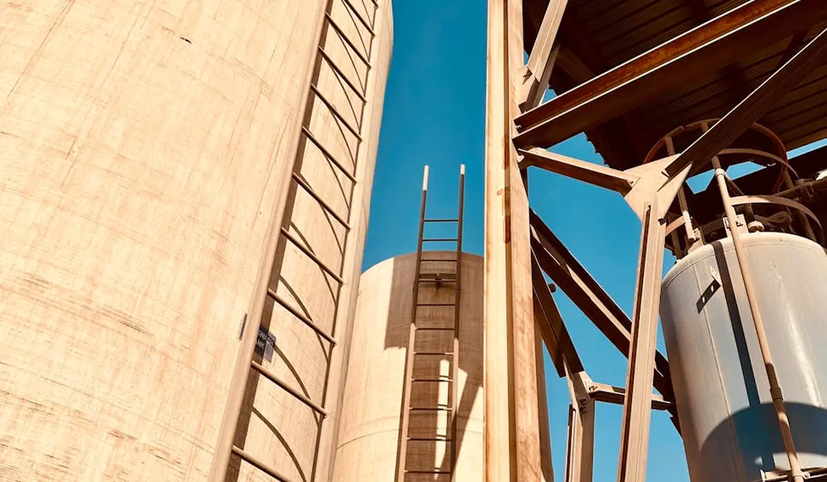 Industrial water treatment facility with tall vertical tanks and metal ladders under a blue sky, representing RO water infrastructure for aquarium use.