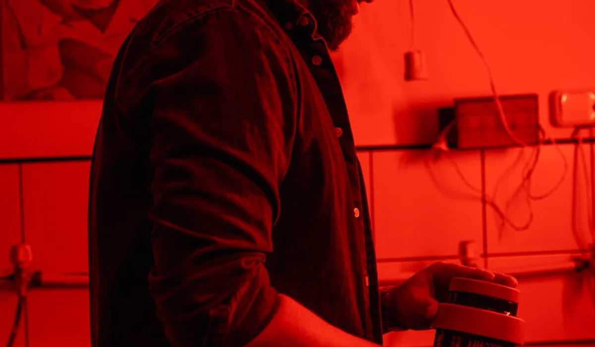 A person in a red-tinted lab holds a bottle on a bench with aquarium gear, illustrating sources of pH fluctuation.