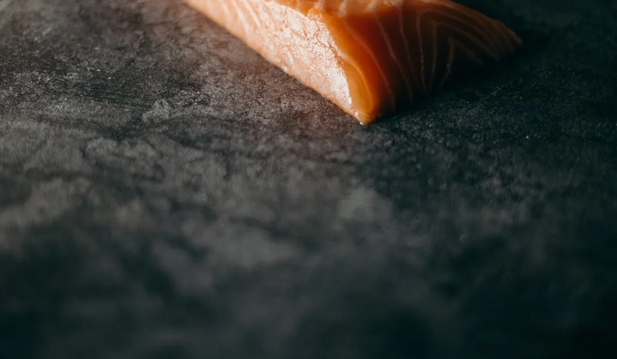 Close-up of a salmon fillet resting on a dark textured surface